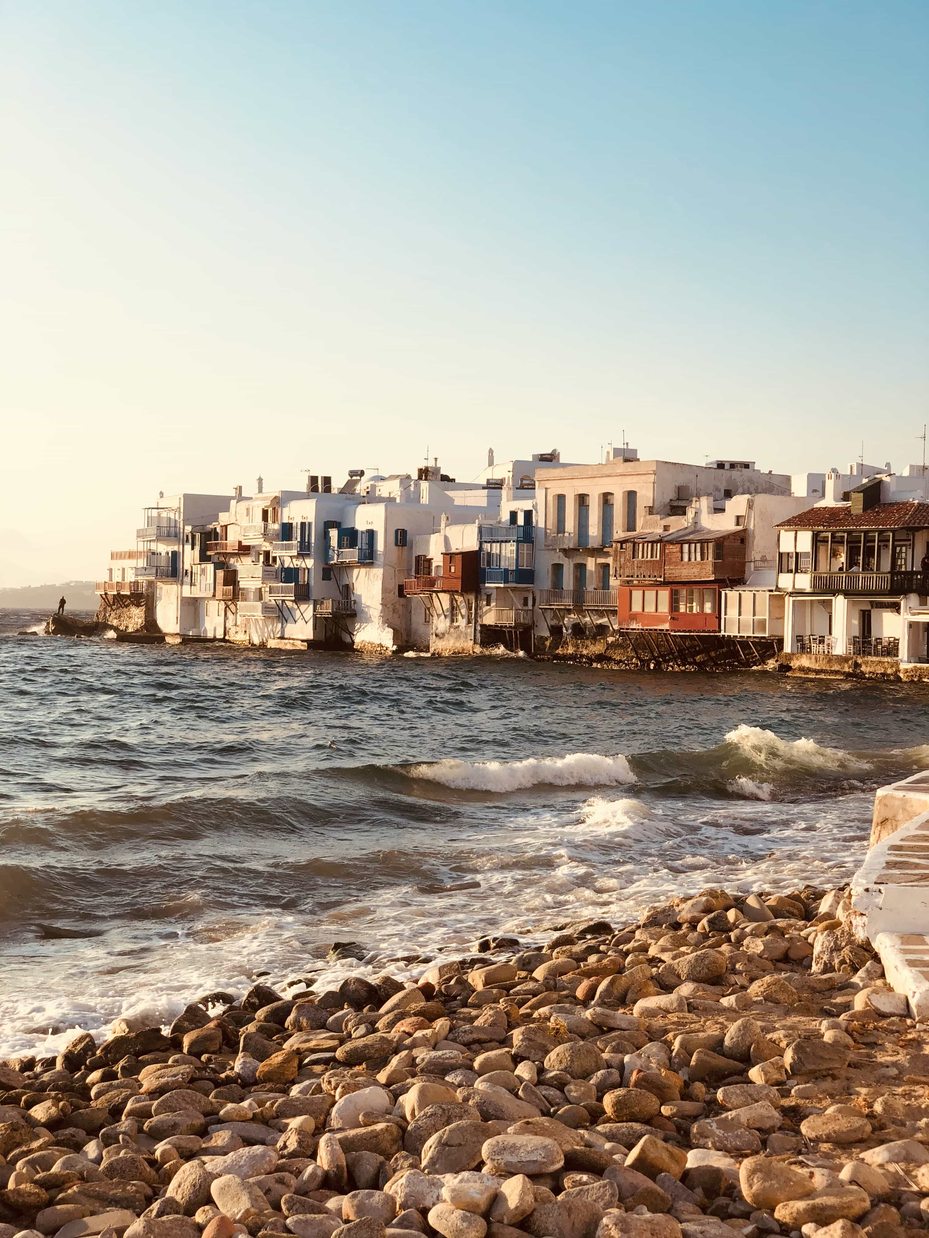 The houses of Little Venice, Mykonos, rising from the sea at golden hour, seen from the pebbled shore