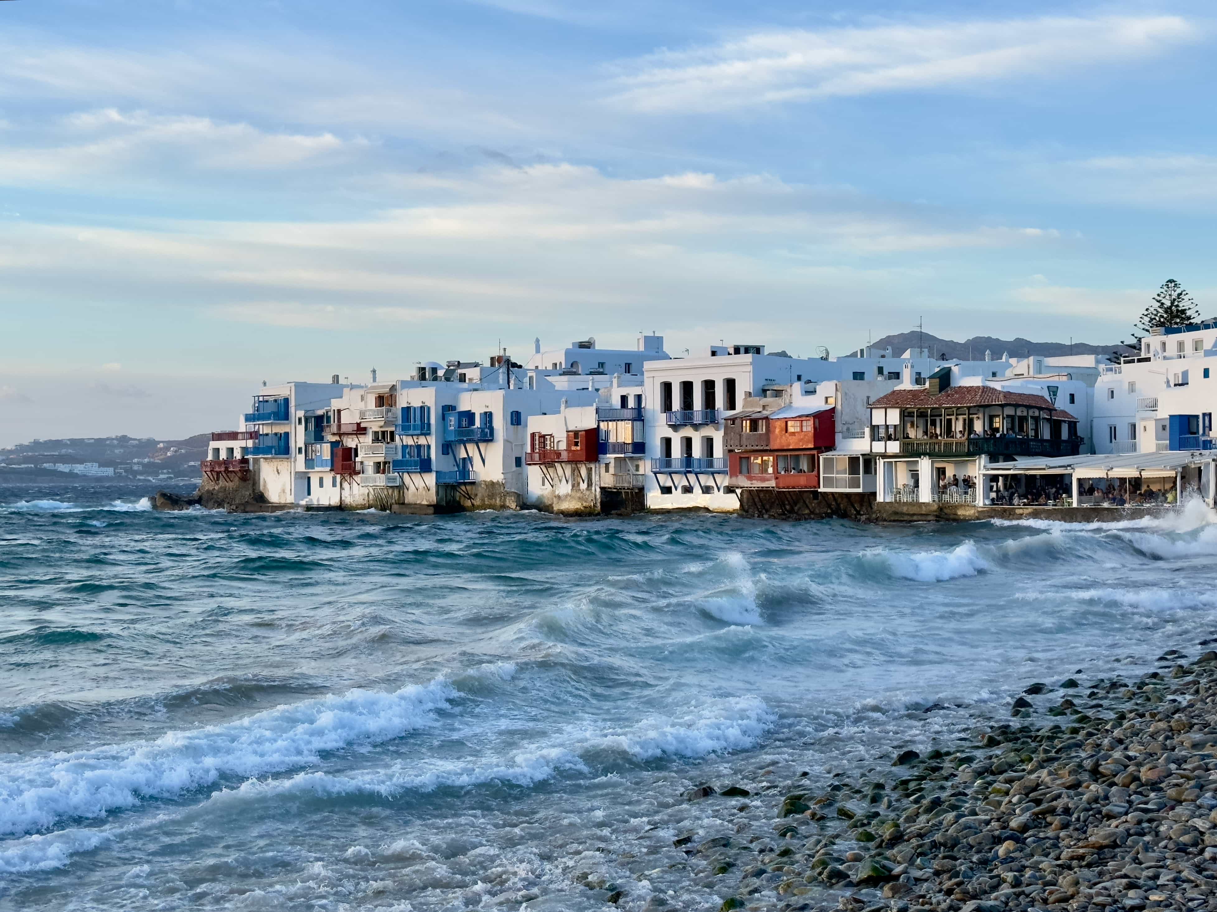 Waves breaking below the balconied houses of Little Venice, Mykonos, at dusk